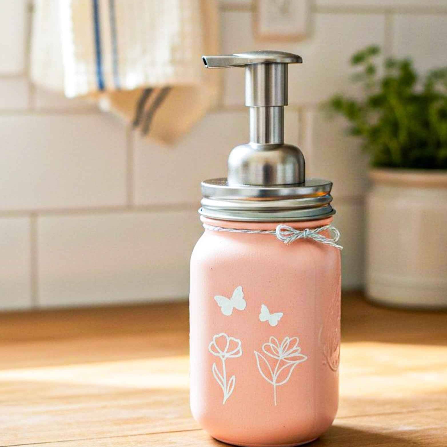 Farmhouse Whimsy butterfly mason jar soap dispenser with peach liquid soap and a butterfly design on a rustic soap jar.